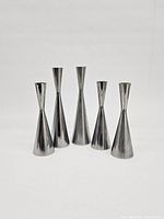Front view of 5 aluminium metal candlestick holders arranged in a row, showing 2 tall and 3 short pieces with a polished metallic surface.