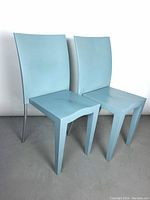 Front view of two light blue Miss Global dining chairs with gray metal legs, placed on a floor against a white wall.
