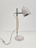 Full side view of pastel pink desk lamp showing the metal shade, chrome and wood vertical stand, and round base.