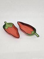 Front view of two chili pepper-shaped bowls showing the red interior and green tops, placed side by side on a white background.