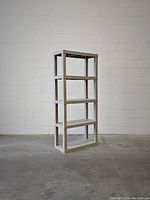 Full view of gray plastic modular shelving unit with four shelves against a white brick wall and concrete floor.