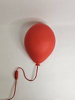 Red balloon-shaped plastic wall lamp mounted on wall, turned off.