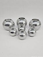 Seven spherical metal candle holders grouped on a white surface, three larger and four smaller shiny silver spheres without candles inside.