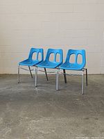 Front view of three blue vintage chairs with fiberglass molded seats and chrome frames