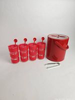Photo of 4 red striped glasses each with a red stir stick, red ice bucket, and metal ice tongs on white background.