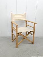 Front angled view of the vintage director's chair showing wooden frame and beige canvas seat and backrest on a gray floor with white paneled background.