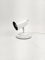 Front angled view of the vintage white metal spotlight table lamp on circular base showing the spotlight head facing forward and slightly down.