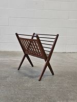 Full side view of the vintage wooden magazine rack on a concrete floor against a white wall.
