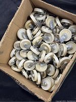 Box filled with over 80 white caster wheels with 2-inch diameter, metal swivel mounts and stems visible.