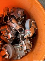 Orange bucket filled with various metal heavy-duty clamps and caster wheels with gray rubber tires.
