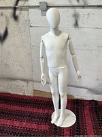 Full view of white child display mannequin standing on round metal base, showing articulated arms and hands with smooth featureless head and torso.