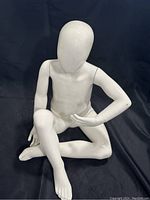 Front angled view of the white sitting child mannequin showing crossed legs and smooth faceless head.