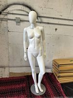 Front view of the full body white female mannequin on metal stand showing entire figure and pose, set against warehouse background.