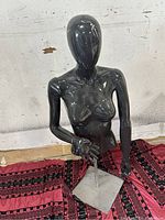 Front view of black glossy female half-body mannequin mounted on metal rod and square base.