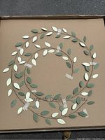 Box containing the 7 metal leaf garland pieces arranged in a circular pattern showing the design and colors (green and white) of the leaves.