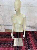 Full view of the off-white female half body mannequin on metal stand against a white wall and patterned floor covering