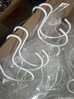 Photo showing several white metal display hooks with curved double-hook design resting on plastic and in box.