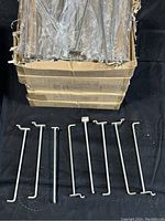 Photo of bulk cardboard boxes filled with packaged metal display hooks, several hooks removed and laid out in front showing length and shape.
