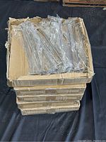 Five cardboard boxes stacked, each containing individually wrapped metal display hooks approximately 10 inches long.