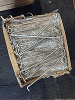 Box containing multiple individually wrapped metal display hooks in bulk packaging.