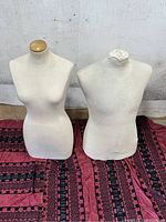 Two torso mannequins, female on left with wooden neck cap, male on right with fabric-covered neck stump, placed on patterned fabric.