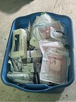 Blue plastic container filled with over 50 pieces of various medical supplies including bandages and wound dressings in original packaging.