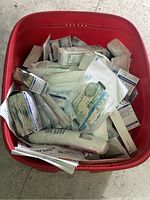 Red storage bin filled with over 50 pieces of assorted medical supplies including bandages and gauze pads in original packaging.