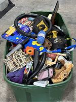 Wide view of green plastic bin filled with a variety of household items including tools, craft materials, accessories, and miscellaneous.