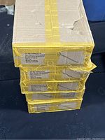 Five stacked cardboard boxes sealed with yellow tape, product labels visible on the side showing item details indicating 8-inch pedestal hooks.