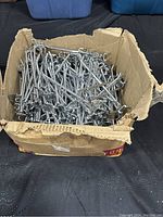 Box filled with over 100 shiny metal pedestal hooks, showing quantity and condition.