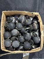 Top-down view of a cardboard box filled with over 60 black plastic ball casters with metal housings, showing the ball wheels and mounting parts.