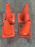 Four orange safety cones, viewed from the front showing wear and dirt marks.