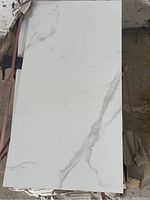 Top view of a stack of rectangular white tiles with grey marble vein patterns, showing tile surface and texture, stacked neatly.