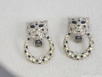 Front view of the pair of silver-tone leopard doorknocker clip earrings showing one missing two stones on the circular ring.