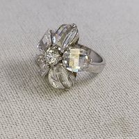 Clear faceted stone flower ring on beige fabric background, showing detailed facets and design