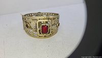 Gold-tone antique bracelet with detailed filigree design and central red rectangular stone