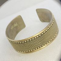Front angled view showing the woven textured pattern and beaded border detail on open metal cuff bracelet.