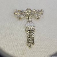 Photo showing front view of the bow brooch with clear rhinestones and white enamel tassel elements on a textile background.