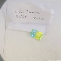 Photo showing the bicolor tourmaline gemstone with handwritten note indicating 32.55ct and approximate size 25x15mm.
