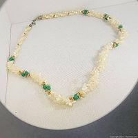 Full view of the handstrung necklace showing the pattern of mother of pearl chips and green stones with bead spacers, displayed on a white background.