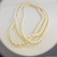 Image showing a single long strand of white pearls looped three times on a cloth display.