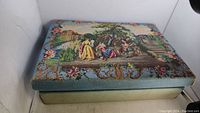 Closed decorative fabric-covered box with classical scene tapestry on the lid.