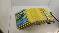 Stack of assorted Pokemon cards with yellow borders, showing the top card featuring a water-themed Pokemon artwork.
