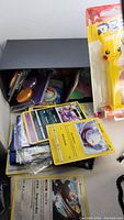 Photo showing assorted Pokemon cards, both loose and in booster packs, with a yellow Pikachu PEZ dispenser in original packaging partially visible.