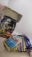 Open box with visible sealed booster packs, loose cards spread outside the box showing various Pokémon types.