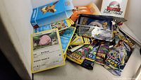 Loose Pokemon trading cards with Charry card on top, several booster packs, and two Pokemon themed boxes including Battle Academy.