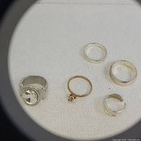 Five rings laid out on white fabric, visible details of stones, bands, and metal tones under magnification.