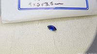 Photo of marquise cut blue sapphire gemstone displayed on a white fabric surface, showing its shape and color.