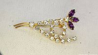 Close-up front view of the antique rhinestone flower brooch showing clear rhinestones and three purple marquise rhinestones on a gold-tone metal stem.