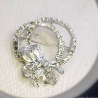 Full view of the silver-toned brooch showing missing rhinestones and bow detail.
